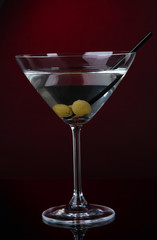 Martini glass with olives on dark red background