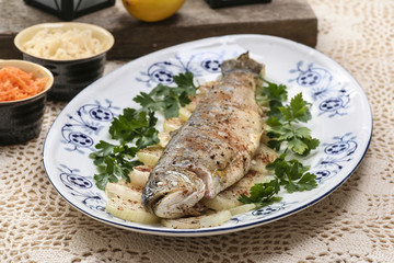 Fish plate in greek tavern. Roasted trout on onion.