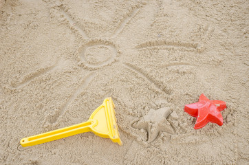 Fototapeta na wymiar Sun drawn in sadn with beach toys next to it
