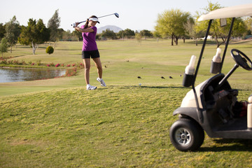 Cute female golfer swinging the ball next to a golf cart