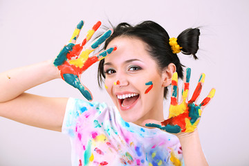 Young pretty painter with hands in paint, on gray background