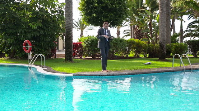 Businessman with tablet computer walking by the swimming pool