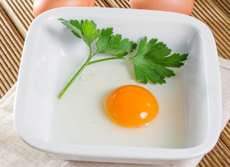 Broken egg in a bowl with parsley