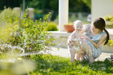 Mother and her baby under a sprinkler