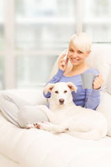 Woman with dog on the sofa holding a mug and phoning