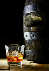 A glass of whiskey with ice and an oak barrel