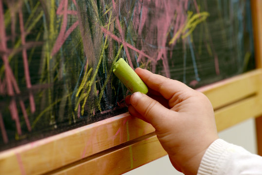 child draws with chalk on a blackboard
