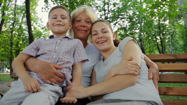 happy grandmother hugs her daughter and grandson on a bench