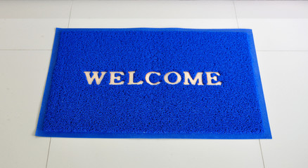 Blue welcome door mat on the floor.