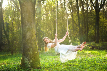 Beautiful bride in white wedding dress swinging in the forest