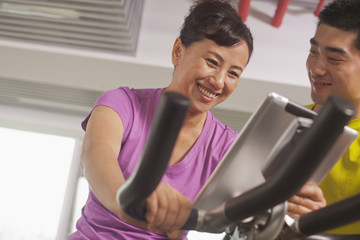 Fototapeta na wymiar Woman smiling and exercising on the exercise bike with her trainer