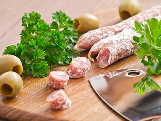 Salami aufgeschnitten auf einem Holzbrett mit Oliven.