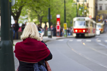 Old woman tourist in Prague photographs a tram