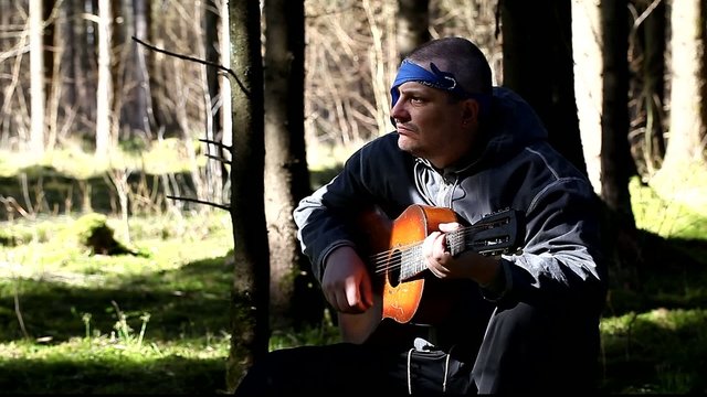 Man  on the stump playing guitar in forest