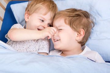 Two little toddler boys having fun in bed