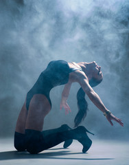 Modern style dancer posing on a studio grey background in fog