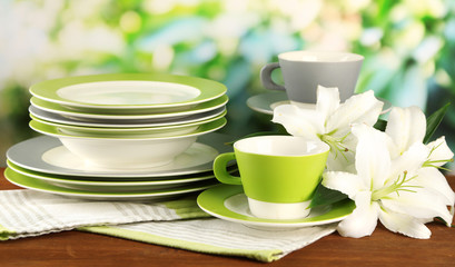 Empty plates and cups on wooden table on green background