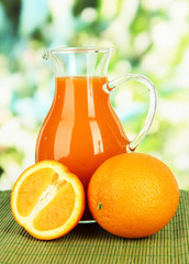 Orange juice in pitcher on table on bright background