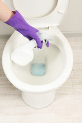 Woman hand with spray bottle cleaning a toilet bowl in a