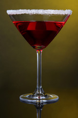 Red cocktail in martini glass on dark yellow background