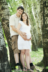 Pregnant wife and her husband in park leaning on trees