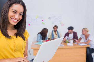 Woman using laptop with creative team working behind her