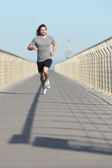 Fototapeta na wymiar Front view of a sportsman running on a bridge