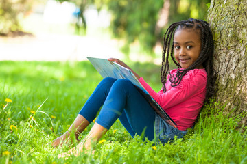 Outdoor portrait of a cute young black little girl reading a boo