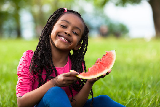 Outdoor portrait of a cute young black little girl eating waterm