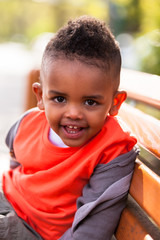 Outdoor portrait of a cute young  little black boy seated on a b