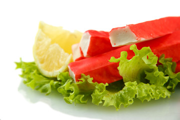 Crab sticks on lettuce leaves with lemon, isolated on white