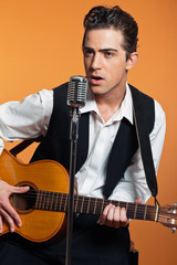 Naklejka premium Retro country singer with guitar wearing black suit. Studio shot