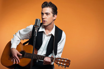Retro country singer with guitar wearing black suit. Studio shot