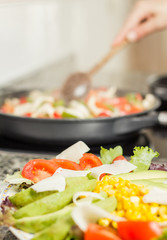Closeup of fresh salad dish and female cooking in a pan