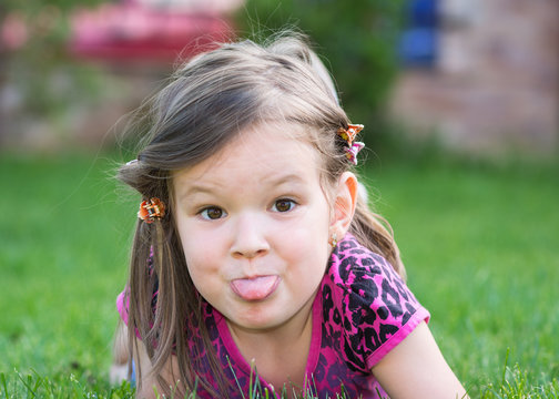 pretty small girl in summer garden showing her tongue
