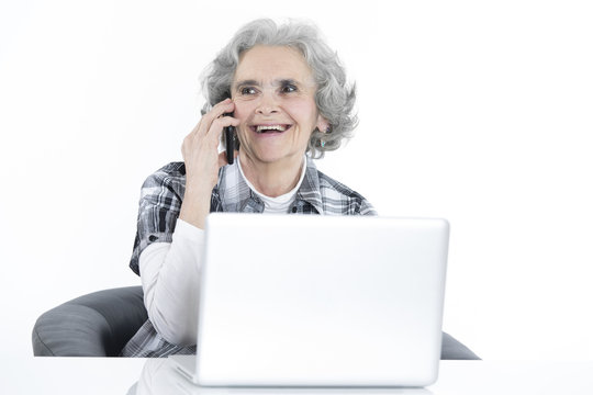 Alte Frau sitzt am Laptop und telefoniert mit dem Handy