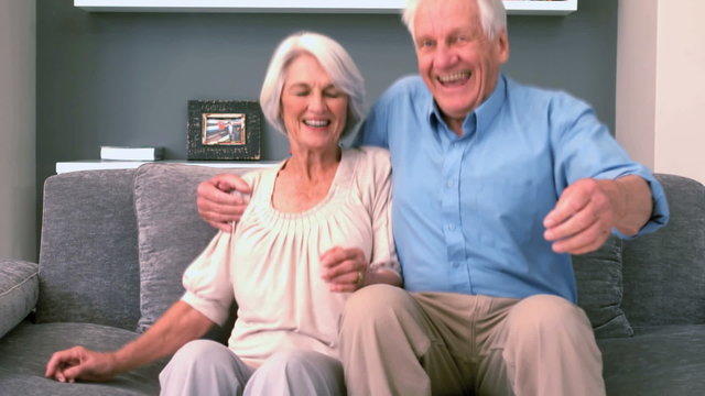 Retired couple sitting down on the couch and smiling