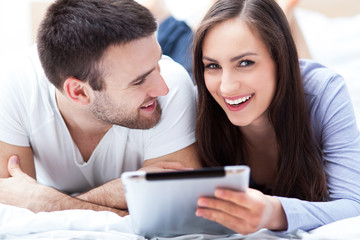 Couple with digital tablet lying on bed