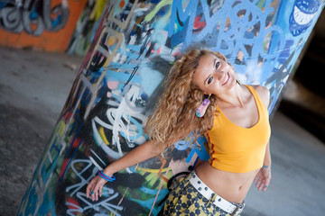Happy hip teenage blonde girl standing by graffiti wall
