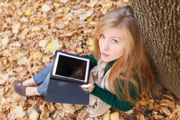 Beautiful young woman with tablet in autumn park