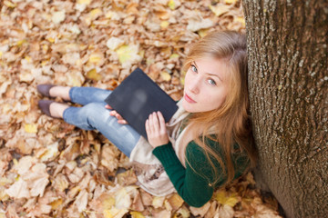 Beautiful young woman with tablet in autumn park