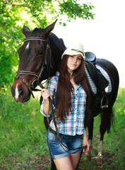 Outdoor portrait of beautiful cowgirl  with horse in green