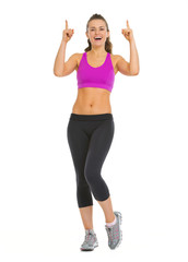 Smiling fitness young woman pointing up on copy space