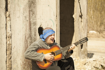 Fototapeta na wymiar Man playing guitar near the destroyed house