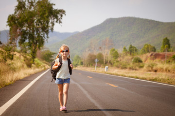 Fototapeta premium little girl with backpack walking on the road