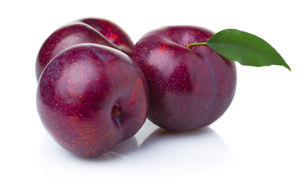 Three ripe purple plum fruits with green leaves isolated