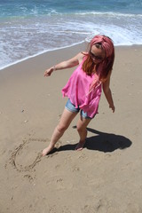 Fototapeta premium Beautiful rehead young woman drawing heart in the sand