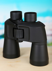 Black modern binoculars on wooden table on blue background
