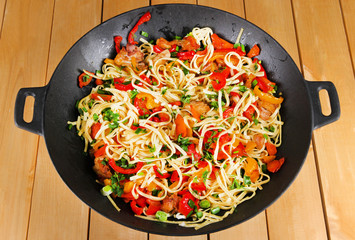 Noodles with vegetables on wok on wooden background