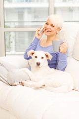 Woman with dog on the sofa holding a mug and phoning